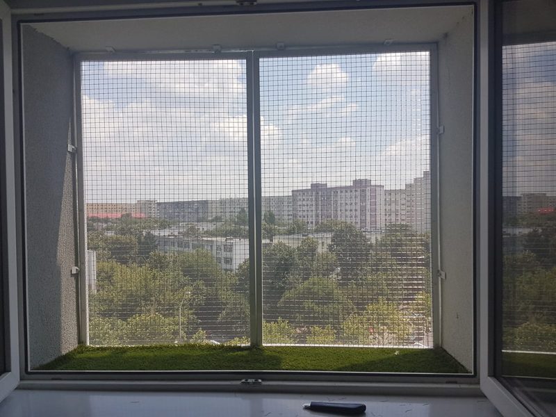 Plasă la perete cu gazon artificial pe pervaz, vedere spre oraș